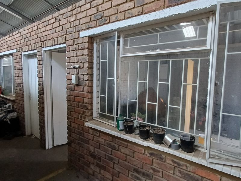 Industrial utility space featuring exposed brick walls, metal security bars on windows, and a high corrugated metal ceiling.