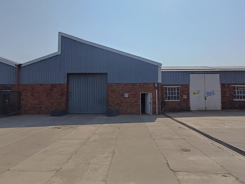 Industrial warehouse exterior featuring brick and corrugated metal facade, roller shutter access, and a large concrete yard area.
