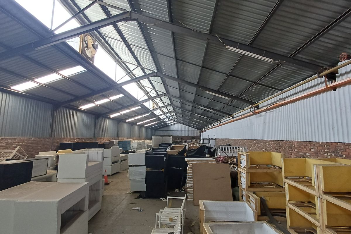 Spacious industrial warehouse featuring high ceilings with exposed steel trusses, skylights for natural light, and durable brick and corrugated metal wall construction.