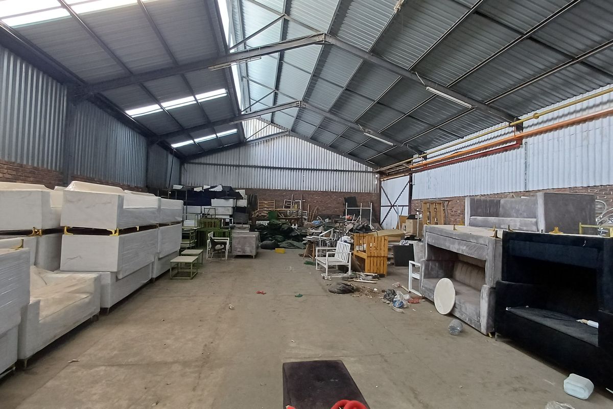 Spacious industrial warehouse unit featuring exposed steel trusses, corrugated metal roofing, brick walls, and durable concrete flooring, suitable for storage or manufacturing operations.
