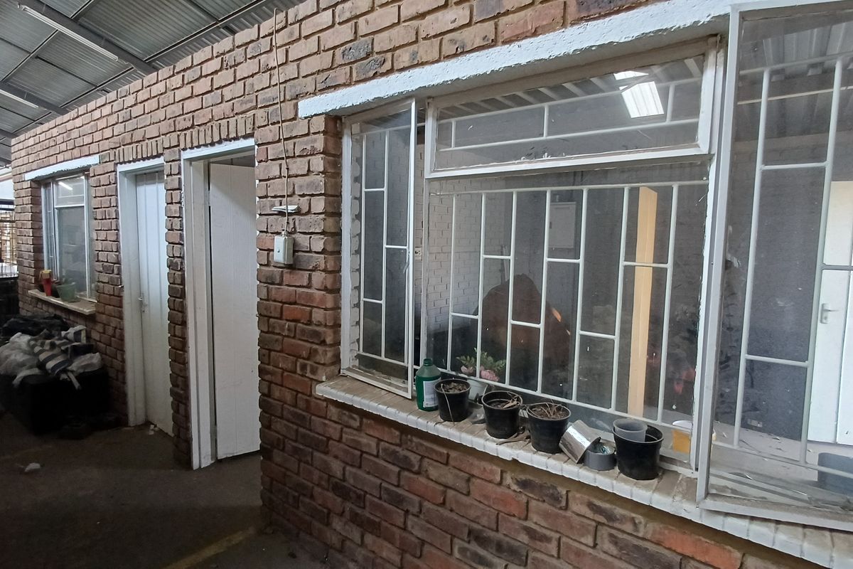 Industrial utility space featuring exposed brick walls, metal security bars on windows, and a high corrugated metal ceiling.
