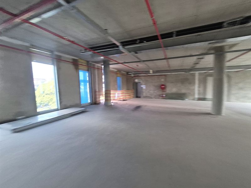 An expansive, unfinished open-plan office space featuring exposed concrete ceilings, structural columns, and large windows, currently in a shell condition.