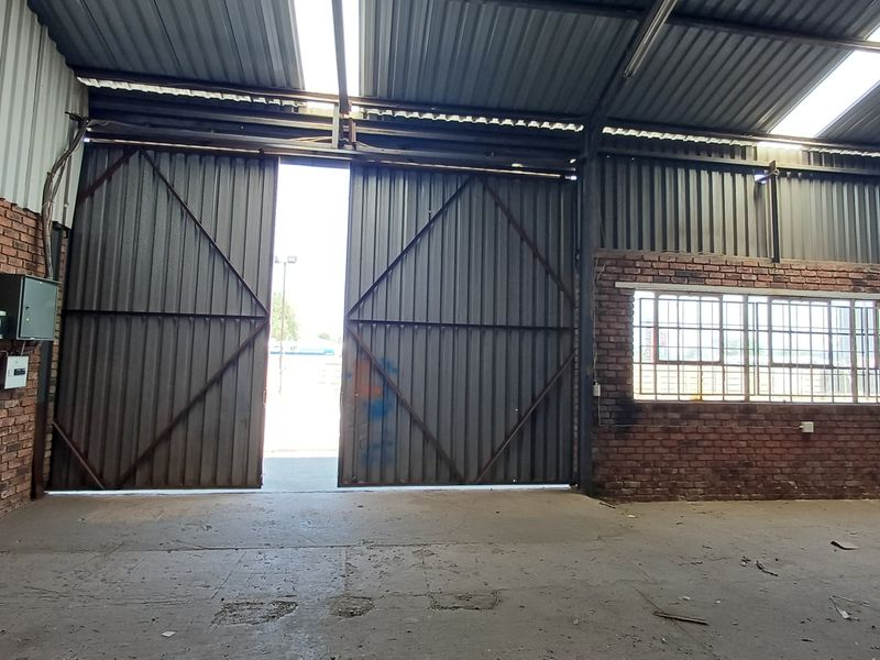Spacious industrial warehouse unit featuring exposed brick walls, high corrugated metal ceilings with skylights, and large sliding access doors.