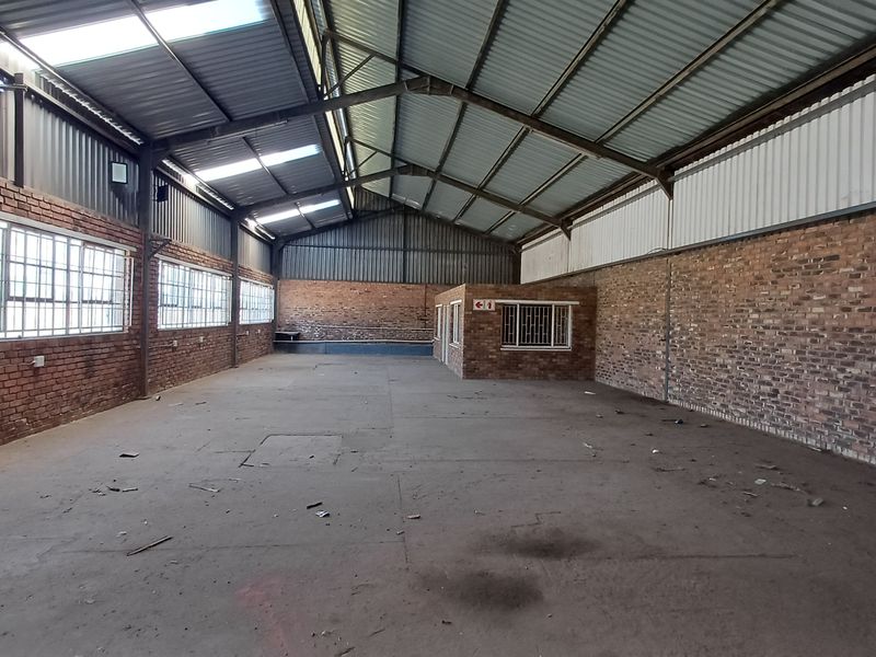 Spacious industrial warehouse featuring exposed brick walls, high steel-truss ceilings with skylights, concrete flooring, and an integrated internal office structure.