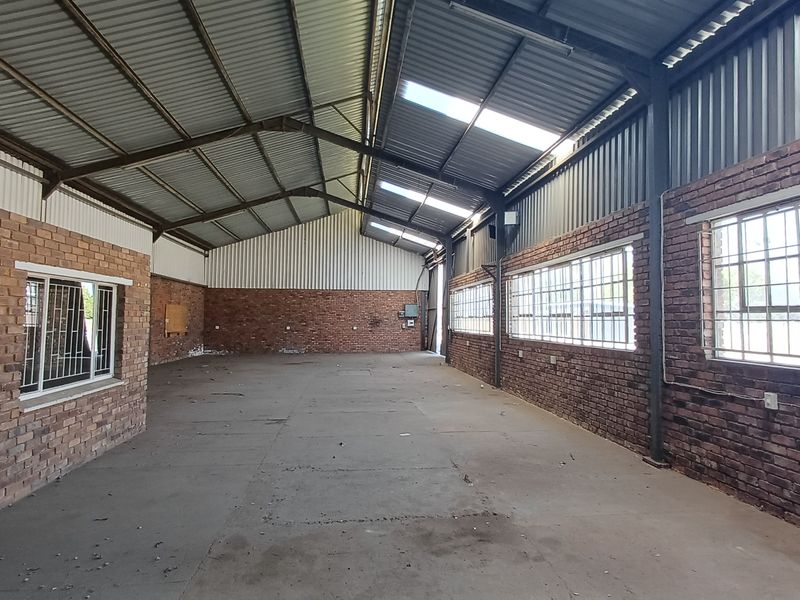 Spacious industrial utility area featuring exposed brick walls, high corrugated metal ceilings with skylights, and large steel-framed windows providing ample natural light.