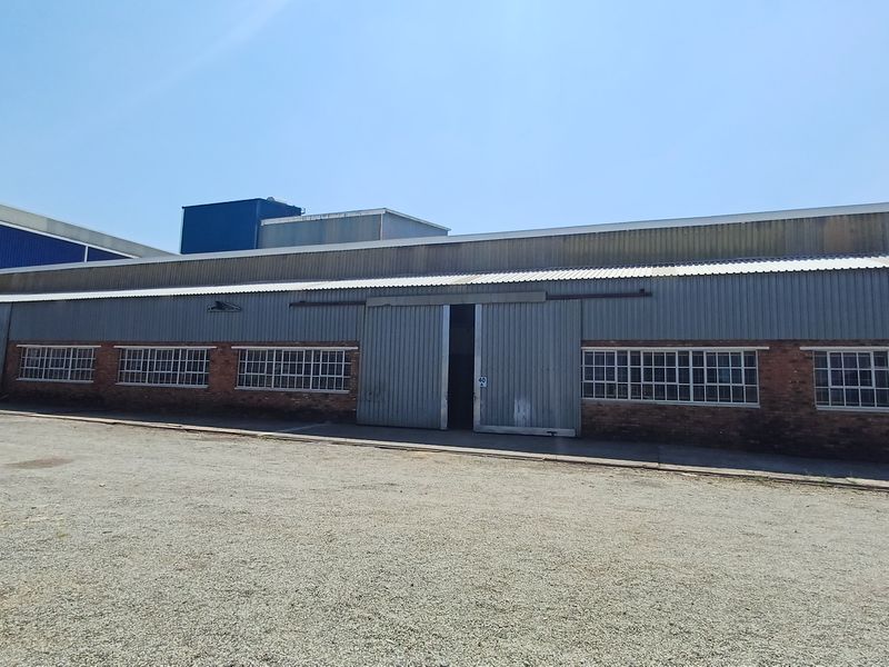Front elevation of an industrial warehouse featuring corrugated metal cladding, brick base, and large sliding access doors.