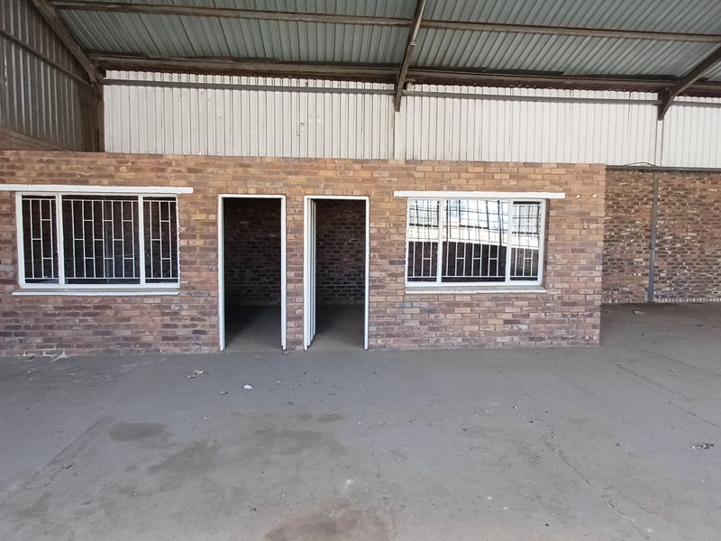 Industrial utility space featuring exposed brick walls, concrete flooring, and a high corrugated metal roof with integrated office or storage rooms.