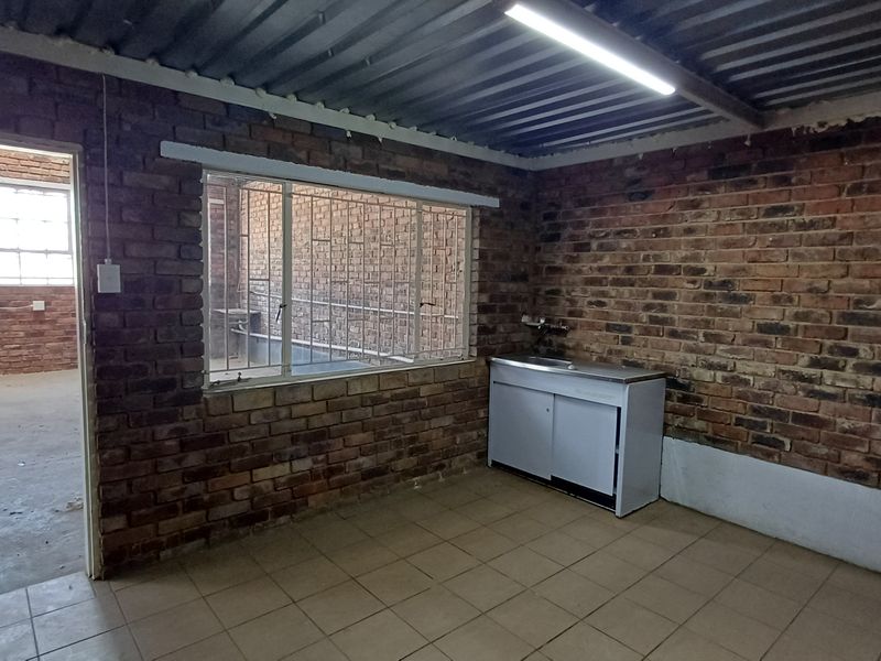 Industrial-style kitchen area featuring exposed brick walls, corrugated metal ceiling, ceramic floor tiles, and a basic stainless steel sink unit.