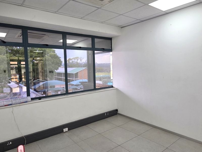 A bright, empty office space featuring large aluminium-framed windows, tiled flooring, and a suspended ceiling with recessed lighting.