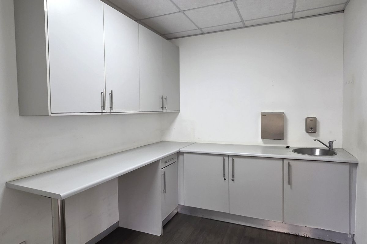 A functional office kitchenette featuring white built-in cabinetry, laminate countertops, a stainless steel sink, and a drop ceiling.