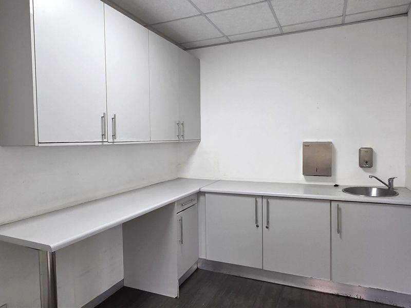 A functional office kitchenette featuring white built-in cabinetry, laminate countertops, a stainless steel sink, and a drop ceiling.