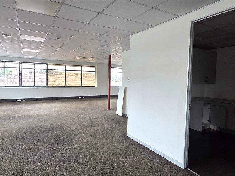 Spacious open-plan office area featuring a suspended ceiling, large windows for natural light, and an adjoining kitchenette space.