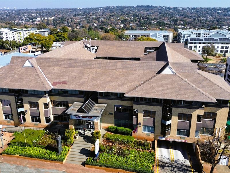 Aerial view of a multi-story office building featuring a tiled roof, brick exterior, landscaped gardens, and a dedicated underground parking entrance.