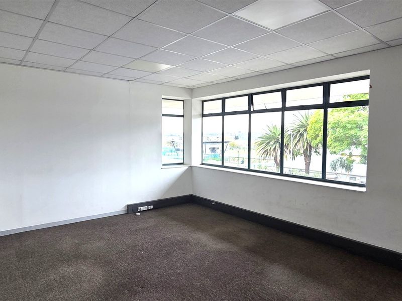 A vacant office space featuring a suspended ceiling, carpeted flooring, and large windows providing natural light and exterior views.
