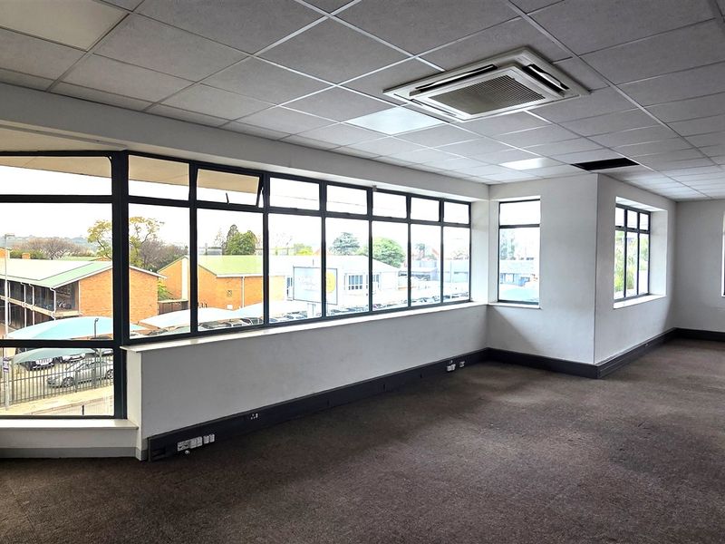 Spacious, vacant office area featuring large windows with natural light, suspended ceilings with integrated air conditioning, and carpeted flooring.