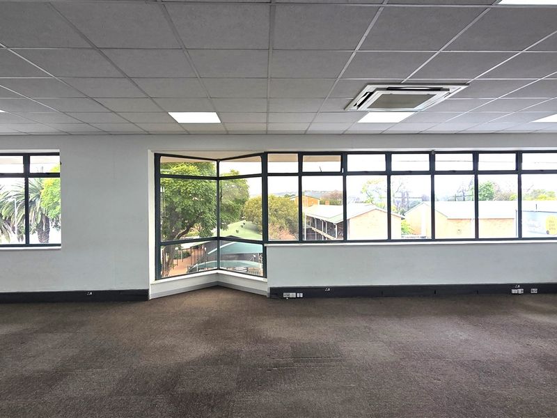 Spacious, open-plan office area featuring large windows with natural light, carpeted flooring, and integrated ceiling-mounted air conditioning.