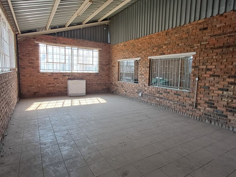 An empty industrial utility space featuring exposed brick walls, tiled flooring, and high-pitched metal roofing with secure window grilles.