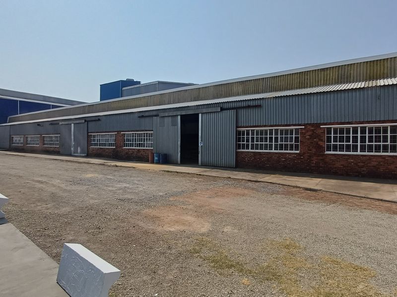Exterior view of an industrial warehouse facility featuring corrugated metal cladding, sliding access doors, and brick masonry construction with a gravel yard.