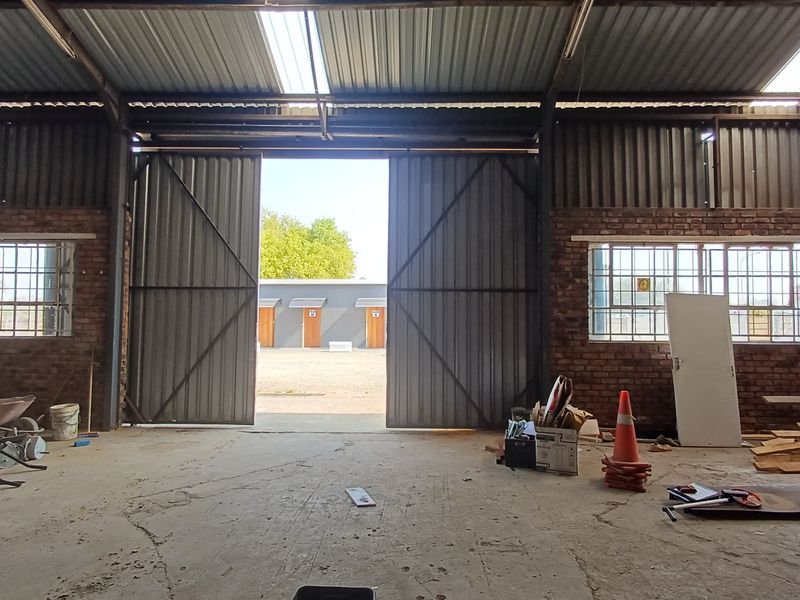 Spacious industrial utility area featuring exposed brick walls, concrete flooring, and large sliding metal doors providing access to the exterior yard.