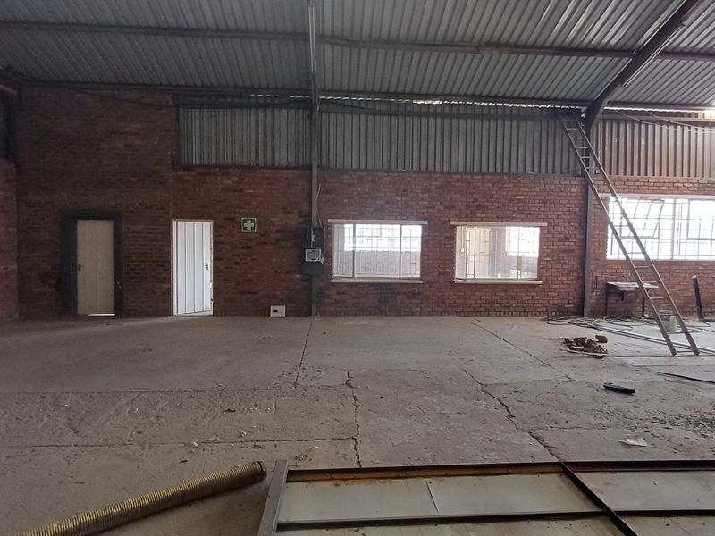 Spacious industrial utility area featuring exposed brick walls, concrete flooring, and high corrugated metal roofing, suitable for warehouse or workshop operations.