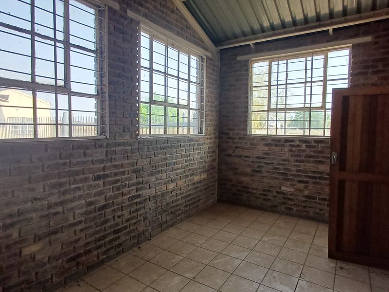 An empty utility space featuring exposed brick walls, tiled flooring, and security-barred windows, suitable for storage or workshop use.