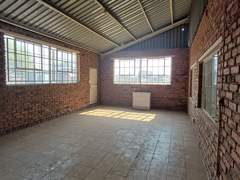 Spacious industrial utility area featuring exposed brick walls, tiled flooring, and large steel-framed windows providing ample natural light.