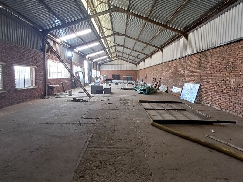 Spacious industrial utility area featuring exposed brick walls, high corrugated metal roofing with steel trusses, and concrete flooring with natural light from skylights.