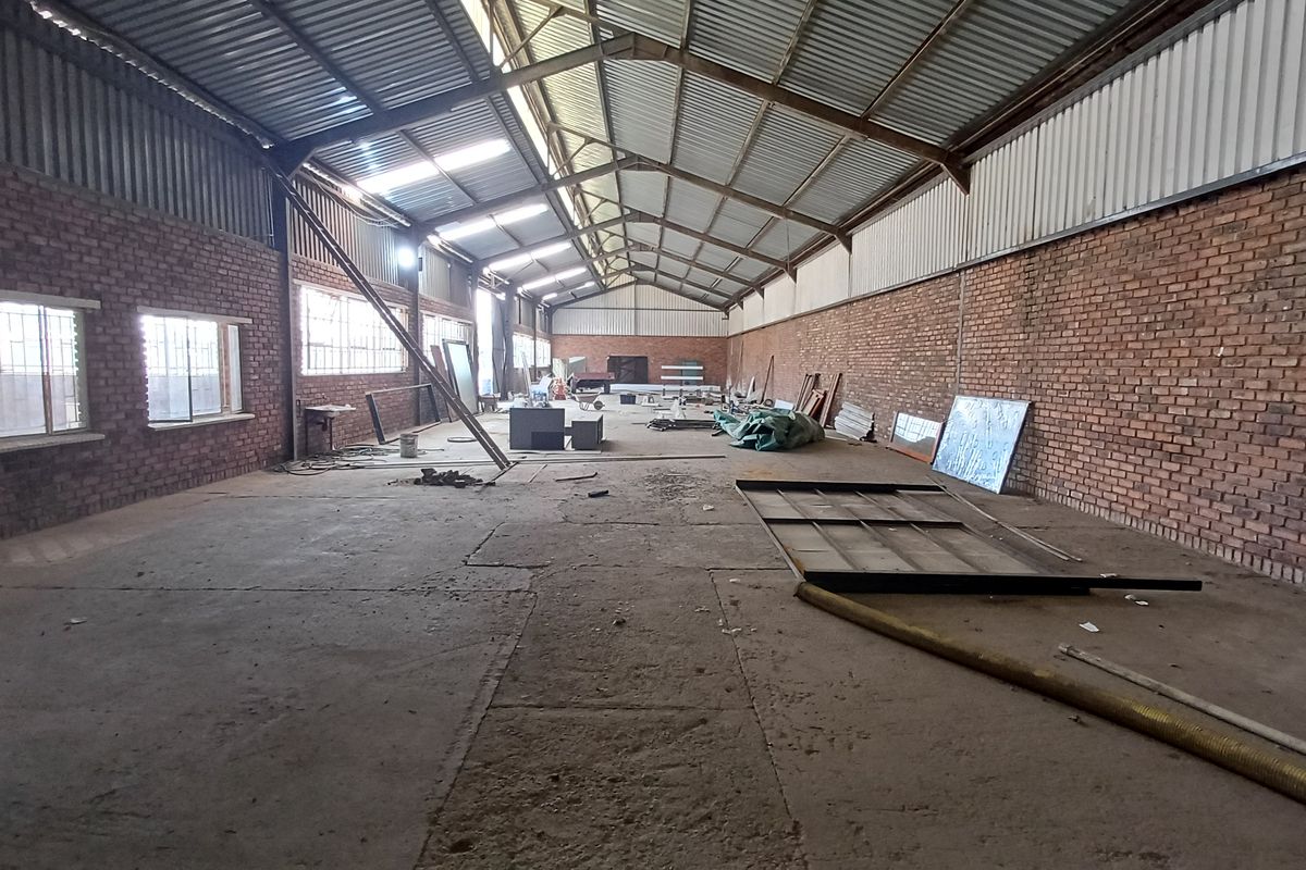 Spacious industrial utility area featuring exposed brick walls, high corrugated metal roofing with steel trusses, and concrete flooring with natural light from skylights.