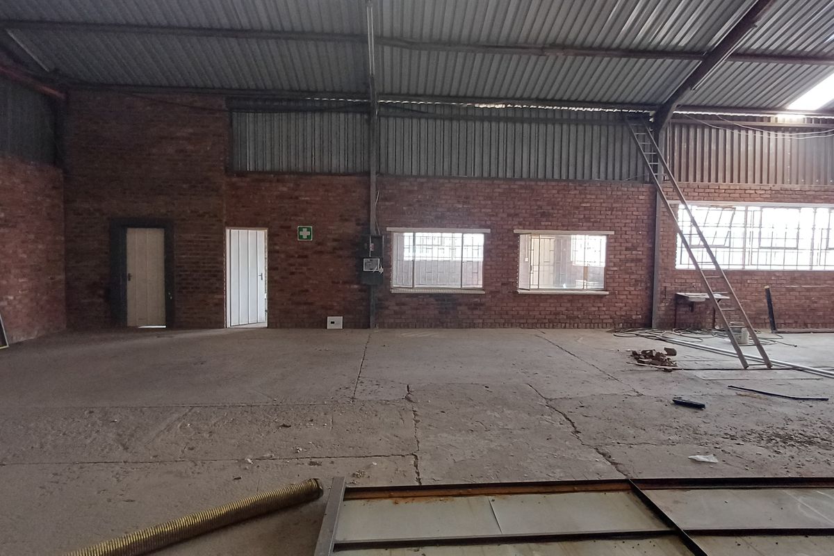 Spacious industrial utility area featuring exposed brick walls, concrete flooring, and high corrugated metal roofing, suitable for warehouse or workshop operations.