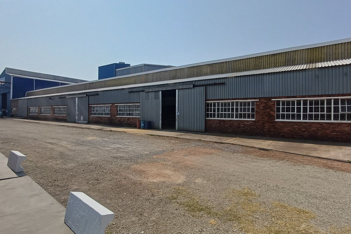 Exterior view of an industrial warehouse facility featuring corrugated metal cladding, sliding access doors, and brick masonry construction with a gravel yard.
