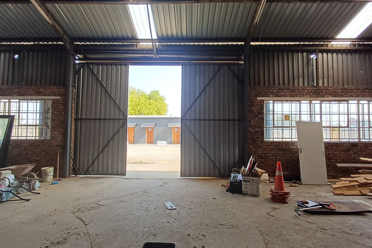 Spacious industrial utility area featuring exposed brick walls, concrete flooring, and large sliding metal doors providing access to the exterior yard.