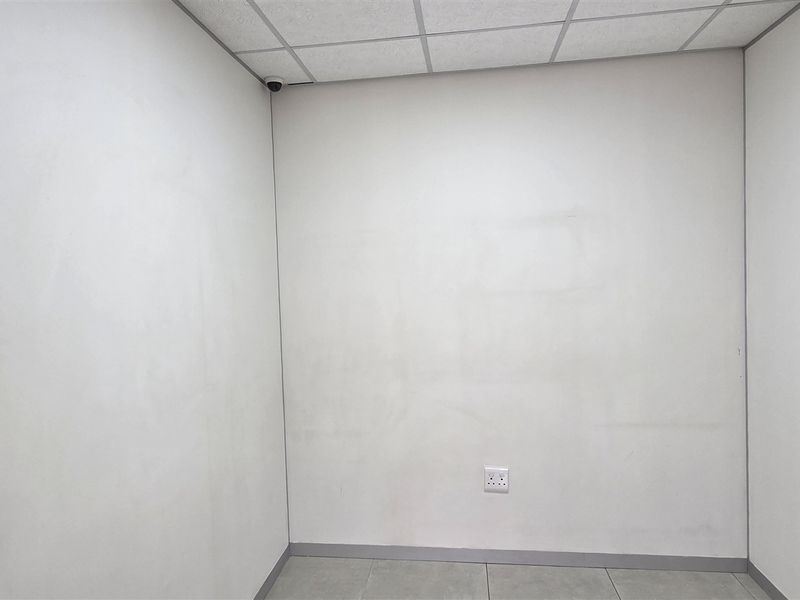 A vacant office space featuring a suspended ceiling, tiled flooring, and wall-mounted security camera, suitable for a professional workspace.