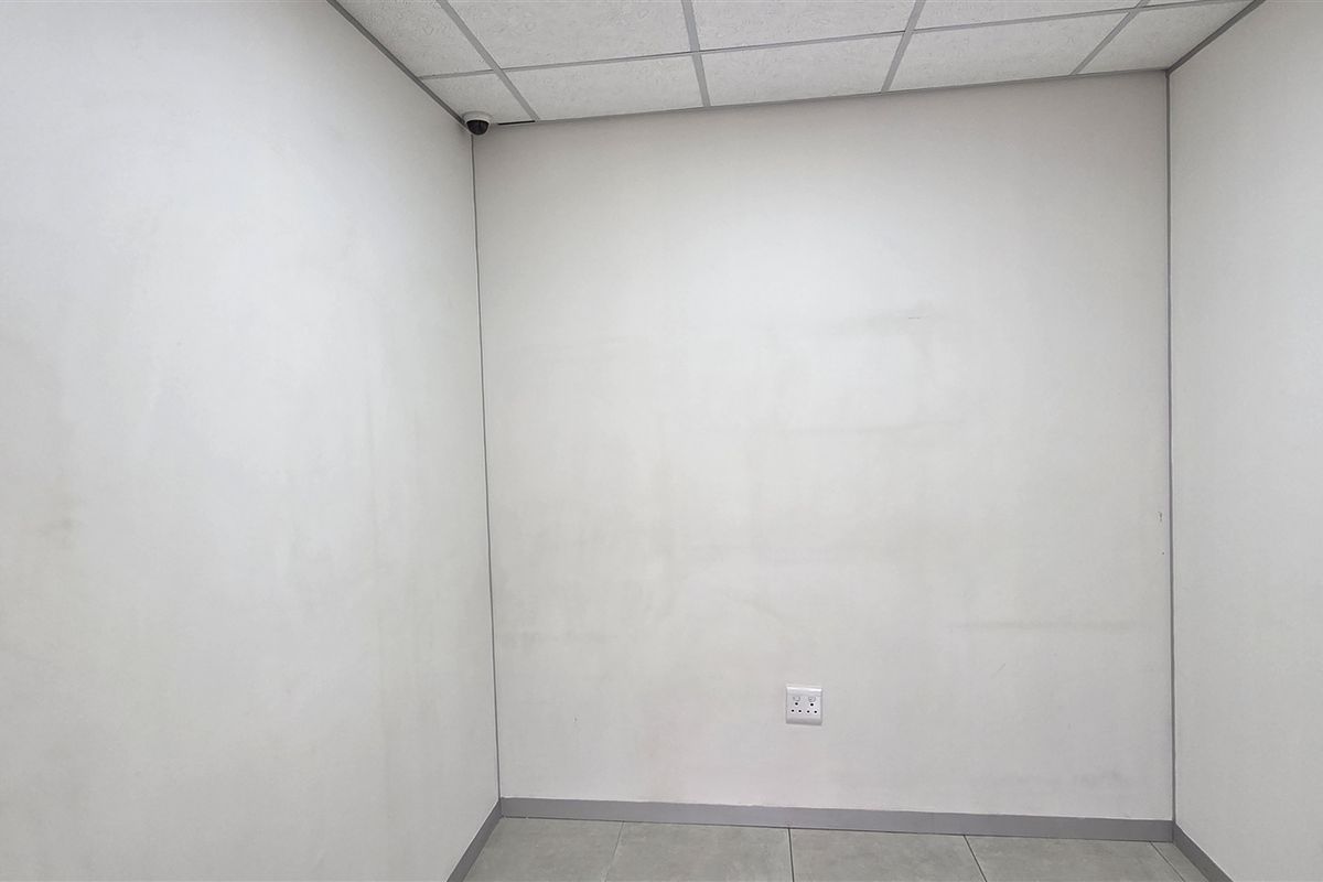 A vacant office space featuring a suspended ceiling, tiled flooring, and wall-mounted security camera, suitable for a professional workspace.
