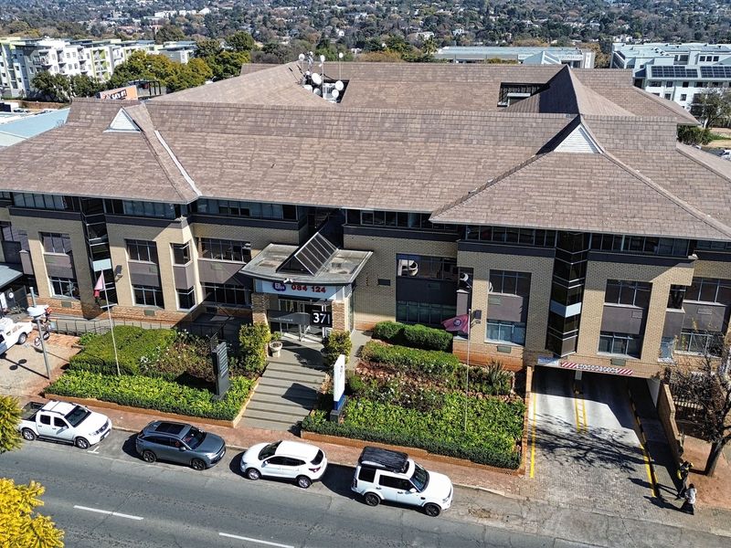 Aerial view of a multi-story commercial office building featuring a tiled roof, brick facade, landscaped grounds, and a dedicated underground parking entrance.