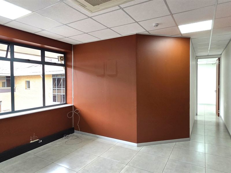 A bright, empty office space featuring tiled flooring, a suspended ceiling with recessed lighting, and large windows providing natural light.