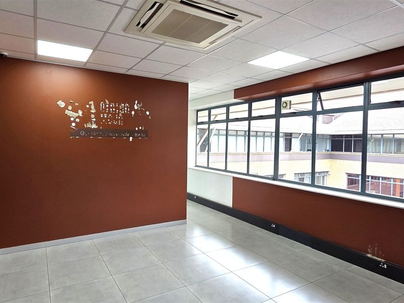 A vacant office space featuring tiled flooring, a suspended ceiling with recessed lighting, integrated air conditioning, and large windows overlooking an internal courtyard.