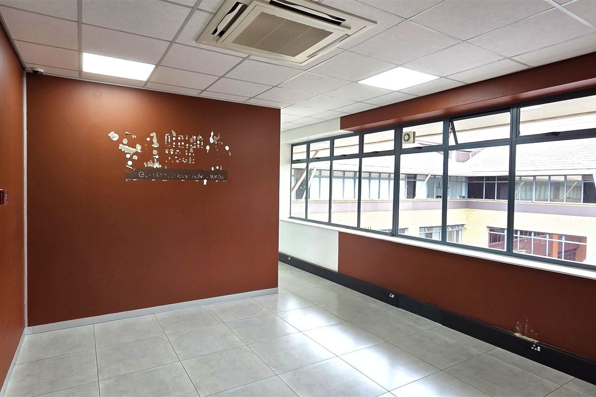 A vacant office space featuring tiled flooring, a suspended ceiling with recessed lighting, integrated air conditioning, and large windows overlooking an internal courtyard.