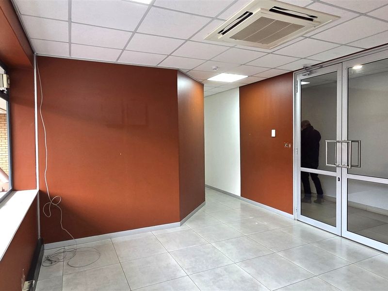 A bright, empty office space featuring tiled flooring, large windows, and a modern suspended ceiling with integrated air conditioning.