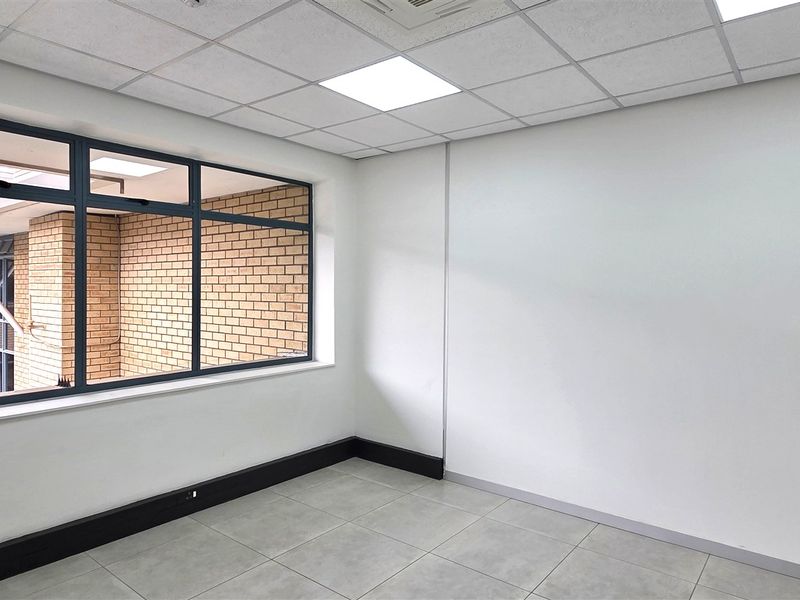 A clean, empty office space featuring tiled flooring, a suspended ceiling with recessed lighting, and large windows overlooking the building exterior.