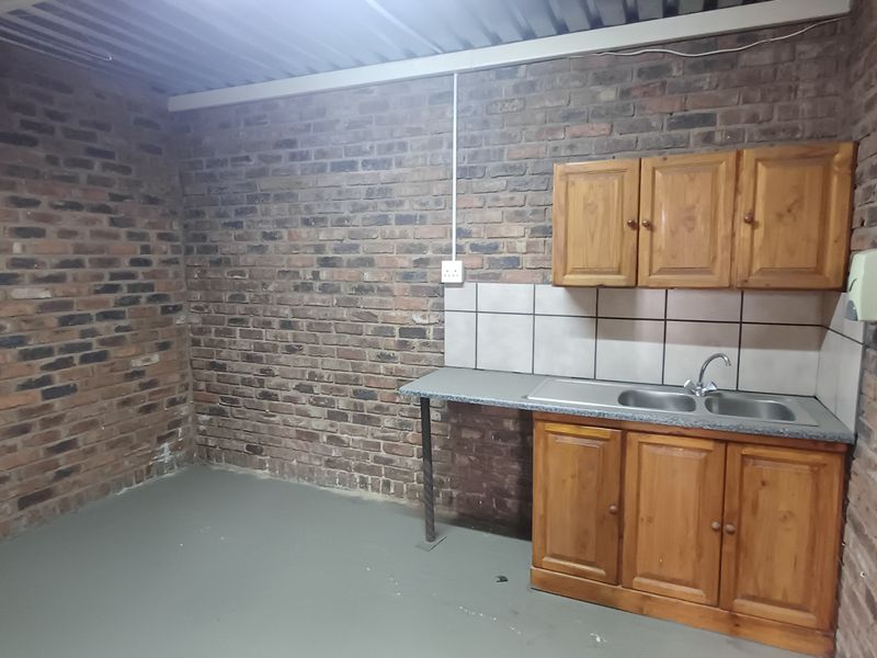 A functional industrial-style kitchenette featuring exposed brick walls, timber cabinetry, a double bowl stainless steel sink, and a corrugated metal ceiling.