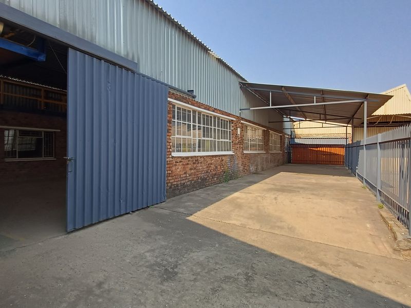 Industrial exterior area featuring a large sliding door, concrete hardstand, steel canopy, and secure palisade fencing, suitable for loading or storage.