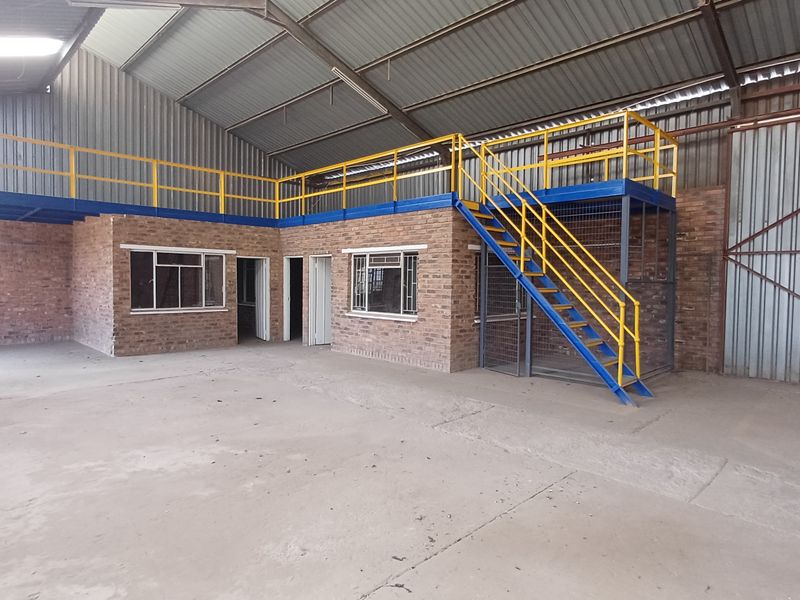 Spacious industrial utility area featuring a mezzanine level with steel staircase, exposed brick walls, and durable concrete flooring under a high corrugated metal roof.