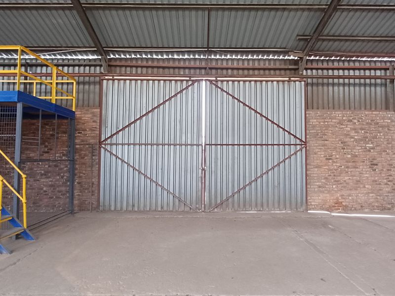 Industrial utility space featuring a large corrugated metal sliding door, exposed brick walls, and a functional steel mezzanine level with staircase access.
