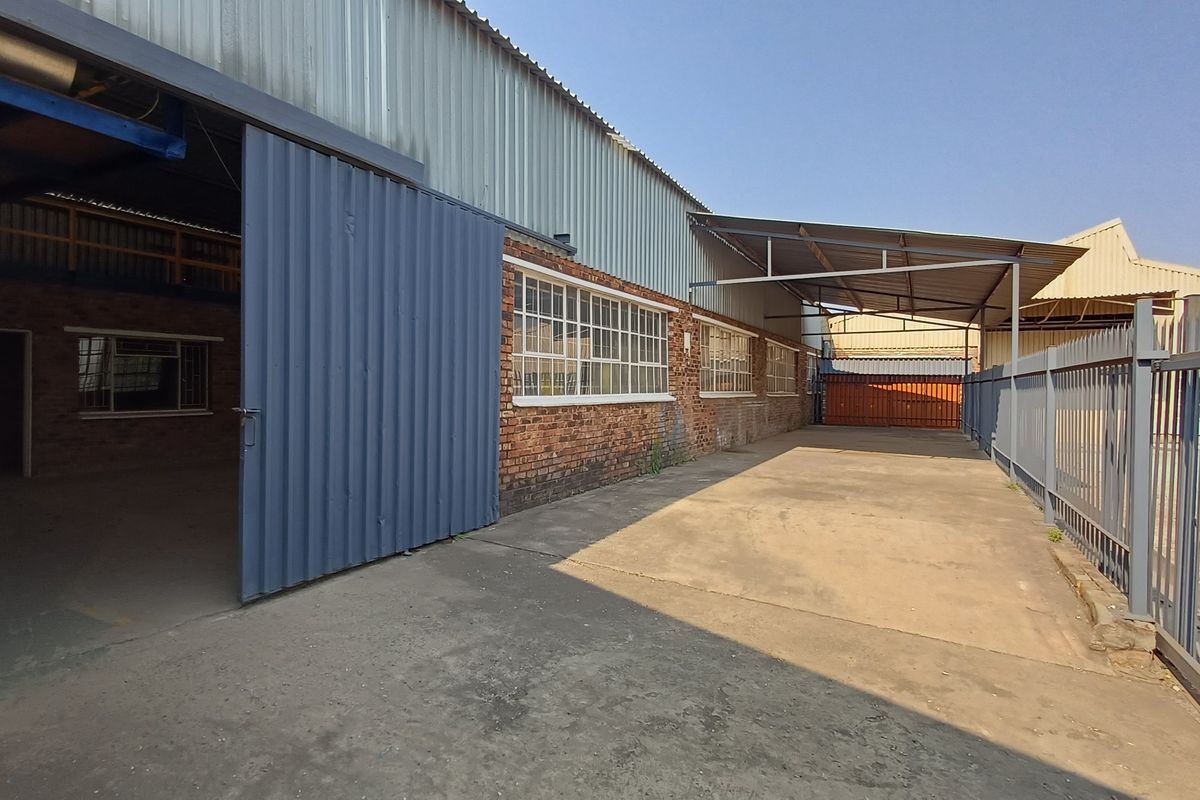 Industrial exterior area featuring a large sliding door, concrete hardstand, steel canopy, and secure palisade fencing, suitable for loading or storage.