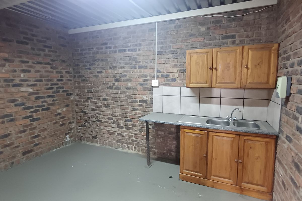 A functional industrial-style kitchenette featuring exposed brick walls, timber cabinetry, a double bowl stainless steel sink, and a corrugated metal ceiling.