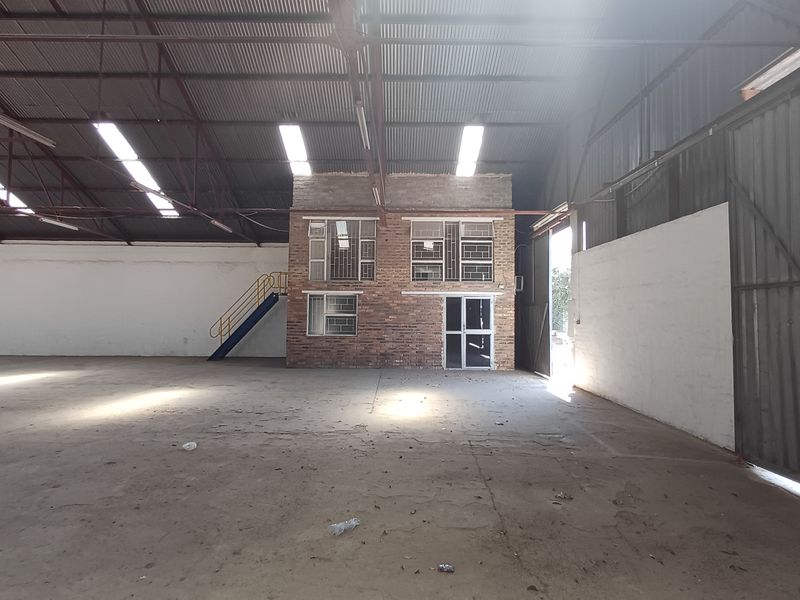 Spacious industrial warehouse featuring high ceilings with exposed steel trusses, concrete flooring, and an integrated two-story brick office block.