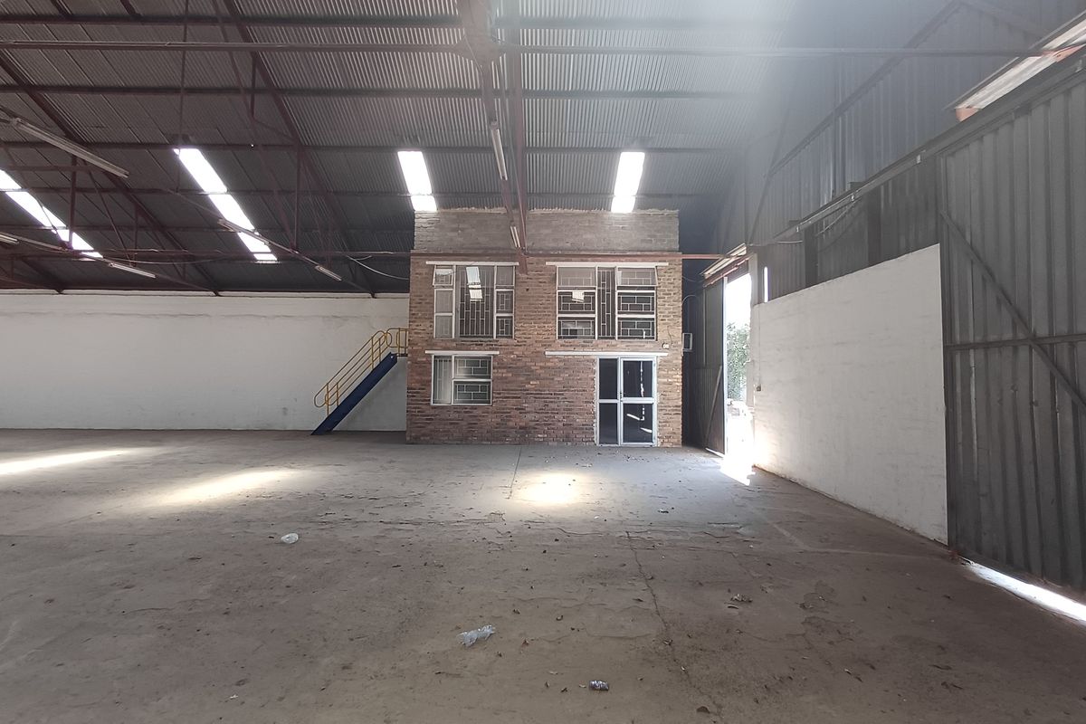 Spacious industrial warehouse featuring high ceilings with exposed steel trusses, concrete flooring, and an integrated two-story brick office block.