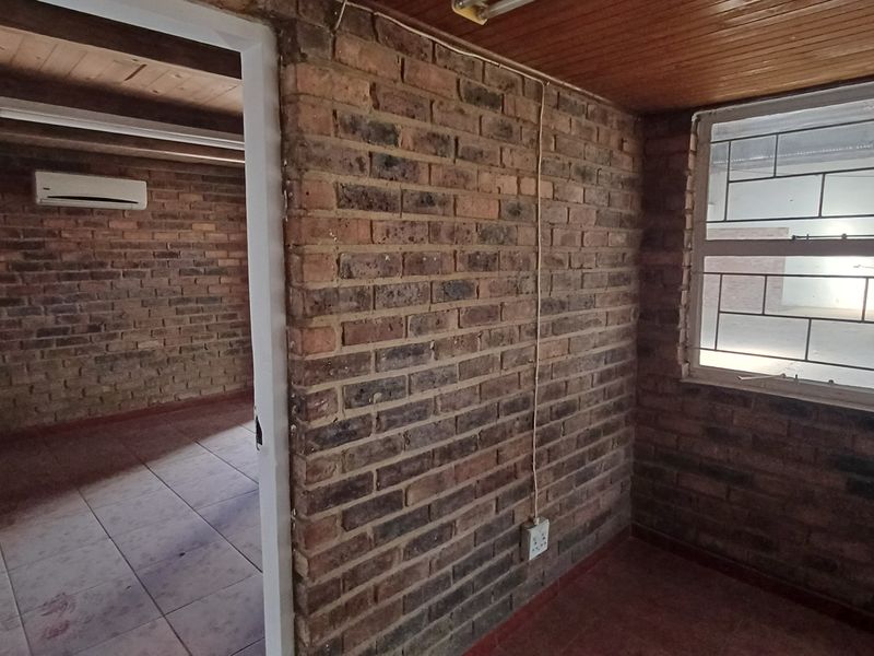An empty office space featuring exposed brick walls, timber ceiling, tiled flooring, and an installed air conditioning unit.