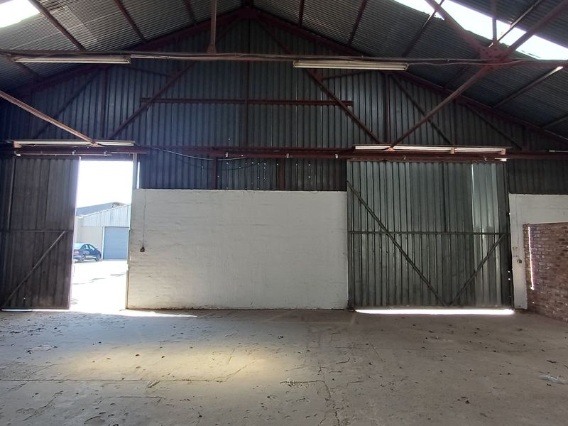 Spacious industrial warehouse unit featuring high ceilings with exposed steel trusses, large sliding access doors, and durable concrete flooring.