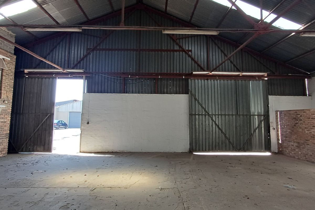 Spacious industrial warehouse unit featuring high ceilings with exposed steel trusses, large sliding access doors, and durable concrete flooring.
